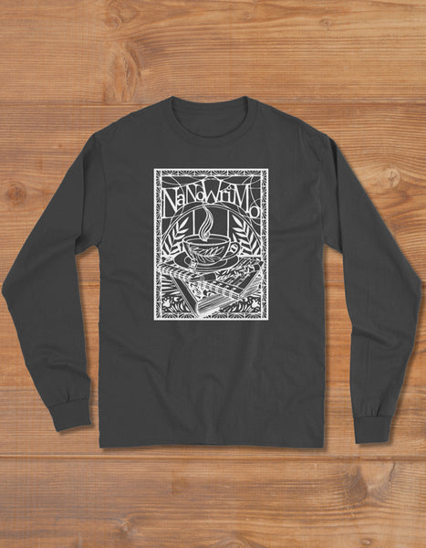 Black crewneck long sleeve shirt featuring a white papercut-style print of a cup of tea, fountain pen, and stack of books. The NaNoWriMo name sits on top of the image. Botanical leaves and filigree fill the background. 